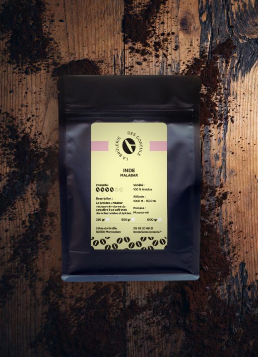 Café Inde Malabar – paquet noir sur fond bois clair, grains jaune doré moussonné – La Brûlerie des Consuls
